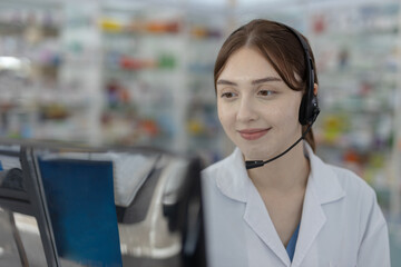 Smiling female pharmacist wearing headset looking at computer screen. Healthcare provider...