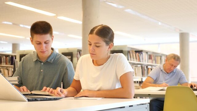 Man in casual clothes asking young lady to be more quiet while she is reading books in the library