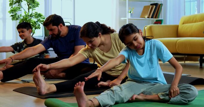 Indian family doing yog asana at home practicing janu shirasana seated head to knee yoga together indoors during calm morning hours inside a modern lavish living space promoting healthy lifestyle