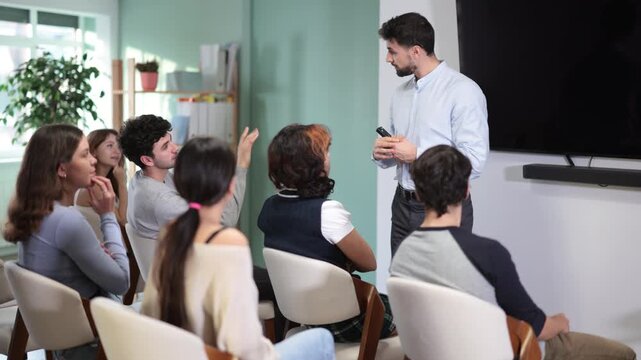 Attentive learners observe male lecturer demonstrating presentation with remote control in interactive educational environment