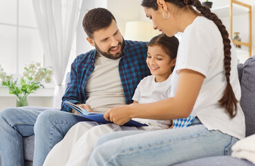 Happy family reading a book together with child girl. Parents and daughter on a sofa at home, as...