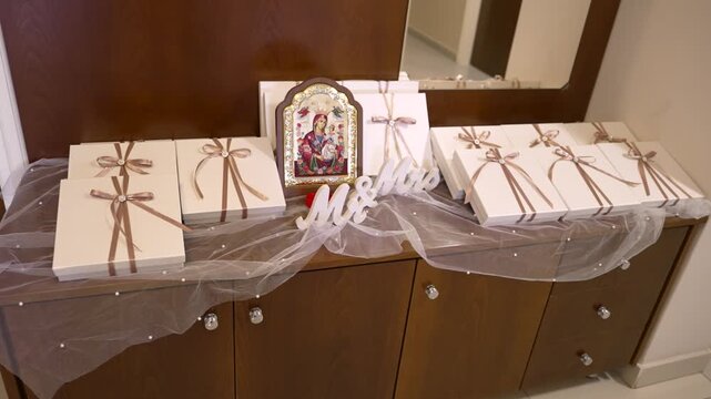 A table is set up with neatly arranged gift boxes tied with ribbons. An image of a saint is placed near the gifts, adding to the festive atmosphere.