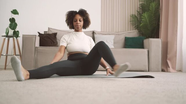 Gymnastics for health of joints and muscles, african woman stretching legs. Beautiful black lady training alone at home, practicing yoga and physical exercise for body shape, developing flexibility