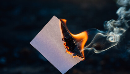 Fototapeta premium Burning paper with smoke rising against a dark background.