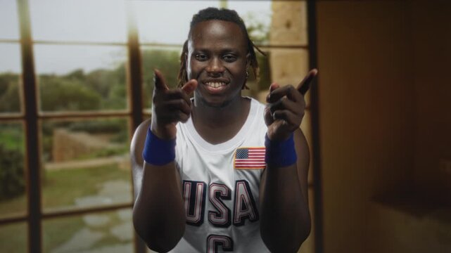 Man wearing usa jersey points both fingers and blows a kiss toward camera in studio; playful confidence.