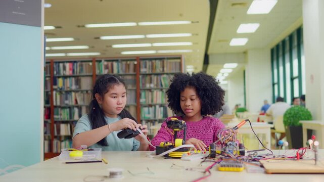 African American and Asian young girls study on robotic project in library. 