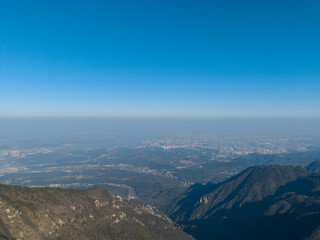 Fototapeta premium Expansive vista from Lushan Mountain in Jiangxi China showing a distant city and hazy horizon under a clear blue sky