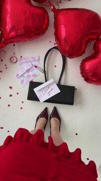 Top view of a woman in a red dress standing near a black handbag and heart-shaped balloons. Valentine&rsquo;s Day lifestyle detail.