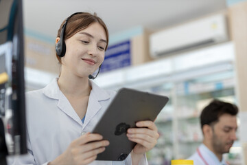 Smiling female pharmacist using digital tablet wearing headset. Young healthcare professional...