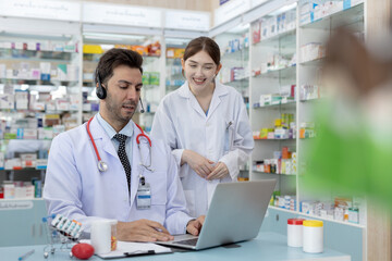 Male and female pharmacists working together using laptop in pharmacy. Healthcare professionals...