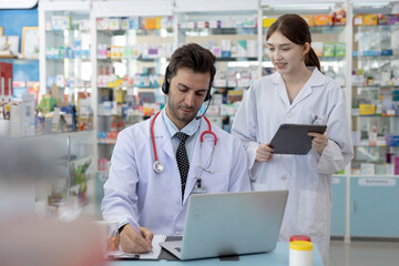 Male and female pharmacists working together using laptop in pharmacy. Healthcare professionals...