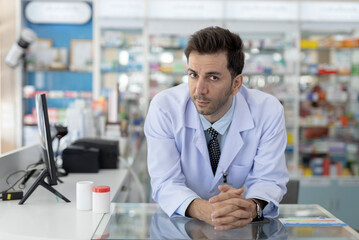 Serious male pharmacist leaning on counter with focused expression. Medical professional showing...