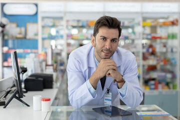 Serious male pharmacist leaning on counter with focused expression. Medical professional showing...