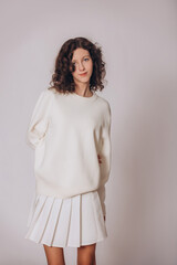 Obraz premium The model is a young beautiful brunette girl with curls on a white background in a white sweatshirt
