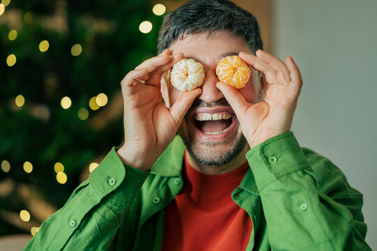 Person playfully holding mandarins over eyes at home during Christmas