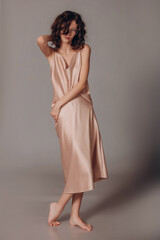 The model is a young beautiful brunette girl with curls on a gray background in a pink silk dress and glasses