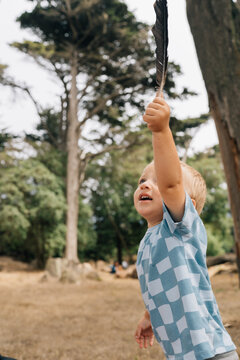 Caucasian Toddler Boy holding black crow bird feather found in park