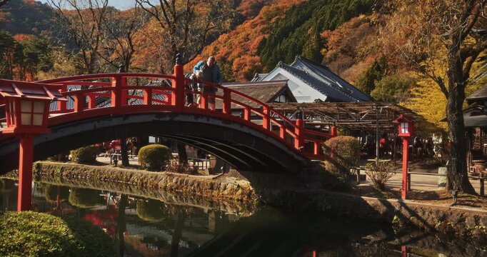 Man and boy looking over ancient Japanese bridge at small stream below during autumn - steady cam shot