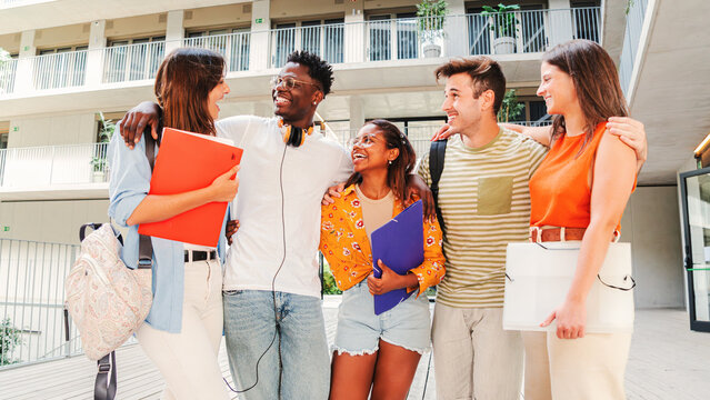 A cheerful gathering of university students engaged in lively conversation while holding colorful folders, showcasing friendship and collaboration among diverse young individuals in a campus setting.