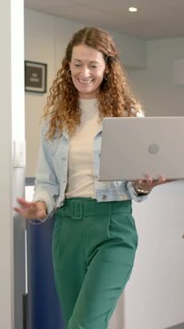 Vertical video: Walking to desk woman in denim jacket explaining work in office with silver laptop
