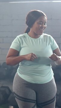 Vertical video: Cueing teal-top woman pumping arms miming taps turning at gym with dumbbells watch