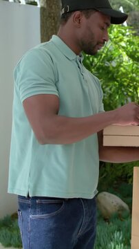 Vertical video: Arriving courier in mint polo holding boxes on porch tapping phone confirming order
