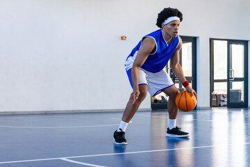 Obraz premium African american teen athlete dribbling orange basketball on gym wearing basketball jersey