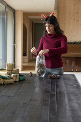 Naklejka premium Hispanic adult woman wearing headband placing pinecones into vase with gifts on table