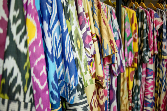 Traditional Uzbek ikat robes and dresses hanging on a rack. Colorful ethnic clothing from Central Asia with vibrant handmade patterns. Authentic silk and cotton apparel