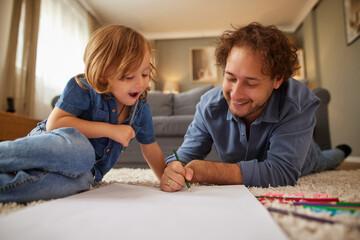 Fototapeta premium Two family members share a joyful moment while drawing on large paper spread on the floor. They laugh and engage in creative activities, surrounded by a warm living room.
