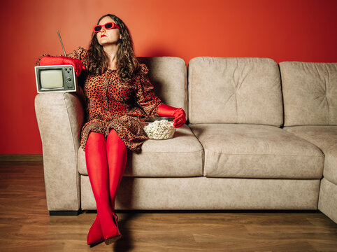 Person in leopard dress with popcorn and retro TV on sofa
