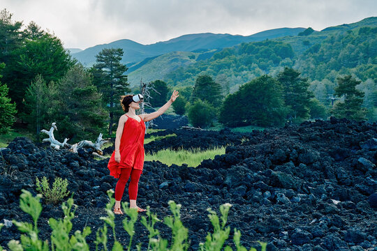 Woman in red dress using VR headset on volcanic Mount Etna landscape