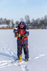 Ice fishing on the river. A fisherman drills a hole with an electric drill for ice fishing.