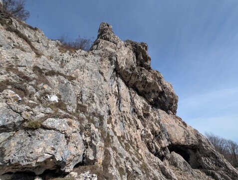 Una maestosa parete rocciosa, caratterizzata da superfici frastagliate e venature naturali scolpite dal tempo. Sullo sfondo, un cielo limpido con leggere velature di nuvole