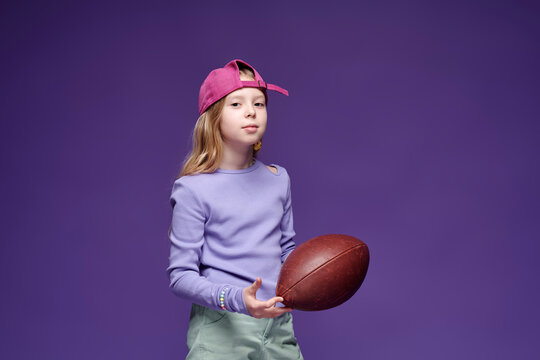 Sporty young girl in y2k streetwear holding rugby ball indoors