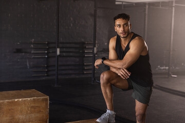 Fototapeta premium Male athlete pausing training kneeling on box beside battle rope wearing tracker in gym, copy space