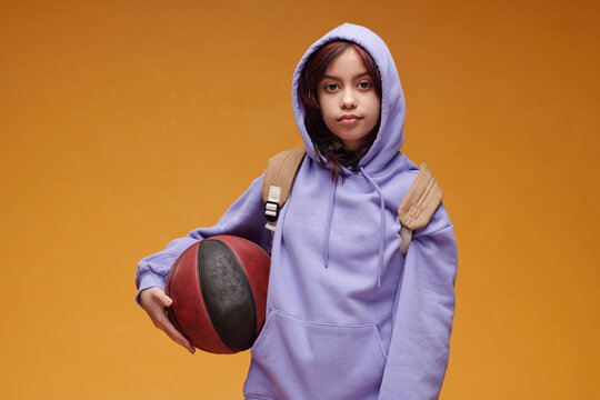 Portrait of student with basketball wearing hoodie and backpack indoors