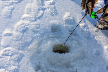 An Ice fisherman uses a winter spinning rod and reel to catch perch or pike in a hole on the frozen surface of a river.