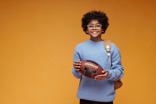 Schoolboy with rugby ball and backpack smiling indoors