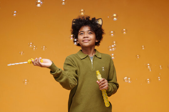 Kid with cat ear headband playing with soap bubbles in studio