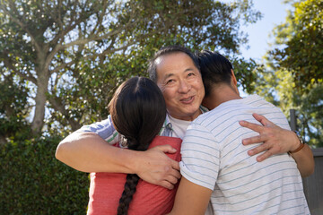 Obraz premium Asian family embracing each other in suburban backyard garden by fence and trimmed hedge