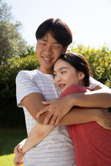 Naklejka premium Asian couple hugging standing on lawn in backyard under sunlight showing braces and earrings