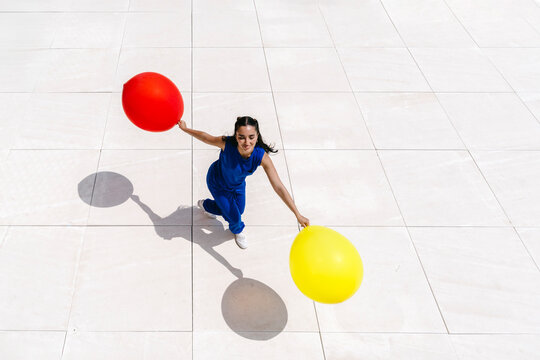 Woman in blue holding red and yellow balloons outdoors on bright floor