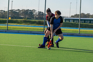 Obraz premium Diverse male field hockey players competing for white ball on turf pitch with sticks