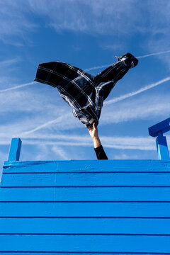 Plaid shirt thrown into the air above bright blue urban fence outdoors