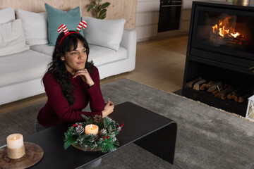 Naklejka premium Woman leaning on black coffee table by fireplace in living room with wreath, candle