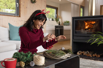 Naklejka premium Asian woman threading berry sprigs onto wreath base on black coffee table in living room