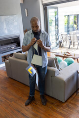 Naklejka premium African american man holding and adjusting paper flags in living room by grey sofa, balloons
