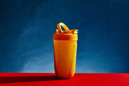 Yellow protein shaker bottle on red tabletop with blue background