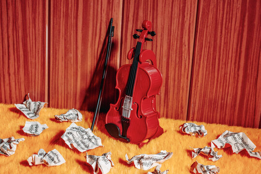 Red toy violin with bow and crumpled simulated sheet music on orange furry floor